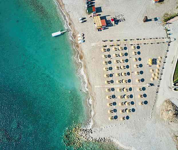 Luftfoto av en strand med parasoller och solstolar bredvid klart blått vatten. (AI-genererad text)