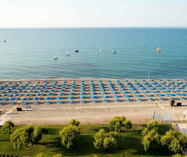 En strand med blå parasoller och solstolar ordnade i rader. (AI-genererad text)