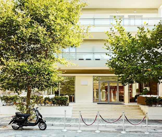 En byggnad med träd i förgrunden och en parkerad scooter framför ingången. (AI-genererad text)