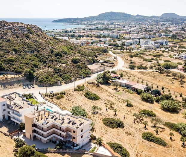 Flygfoto av en byggnad nära en bergskulle med utsikt över en stad och havet. (AI-genererad text)