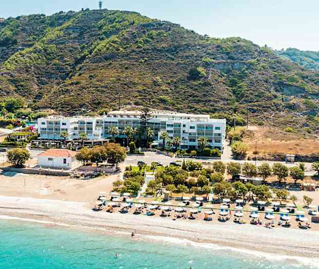 Strand med solstolar och parasoller, bakom ligger en byggnad vid en bergsutlöpare. (AI-genererad text)