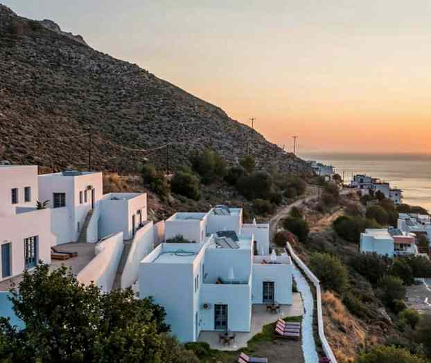 Vitmålade hus på en sluttning vid solnedgången, med utsikt mot havet. (AI-genererad text)