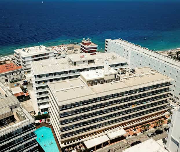 Flygbild över hotell och en strand vid havet. (AI-genererad text)