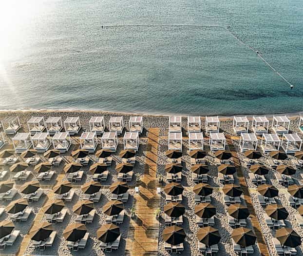 En vy över en strand med rad av parasoller, solstolar och vita solskydd nära havet. (AI-genererad text)