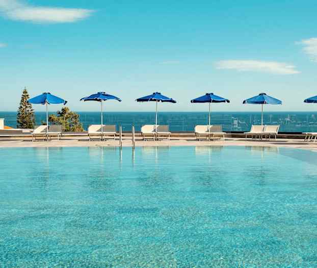 Utomhuspool med blå parasoller och utsikt över havet. (AI-genererad text)
