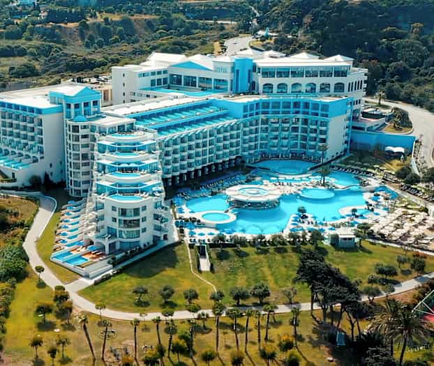 Stor hotellbyggnad med flera blå balkonger och pooler, omgiven av grönska. (AI-genererad text)