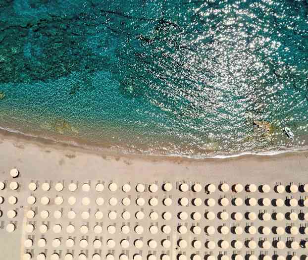 Strand med parasoller sedd från ovan nära klart vatten. (AI-genererad text)