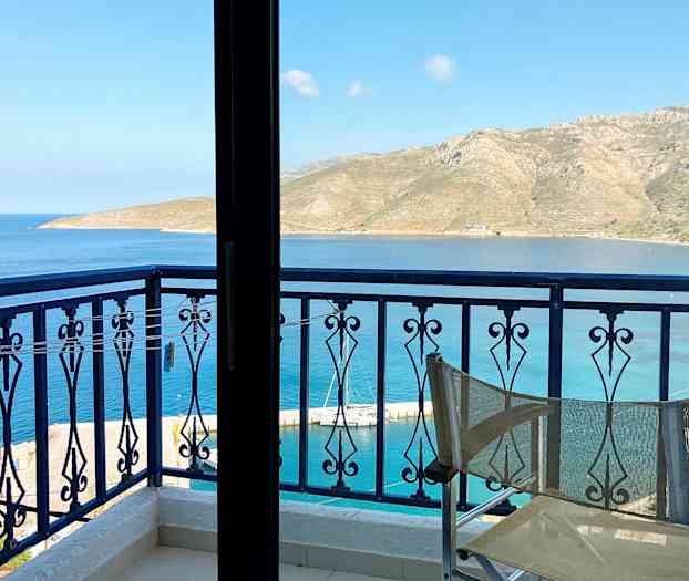 Utsikt från en balkong med en stolsrygg i förgrunden, mot havet och berg i fjärran. (AI-genererad text)