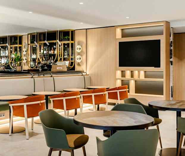 En hotellbar med sittgrupper och bord, omgärdad av en modern och ljus interiördesign. (AI-genererad text)