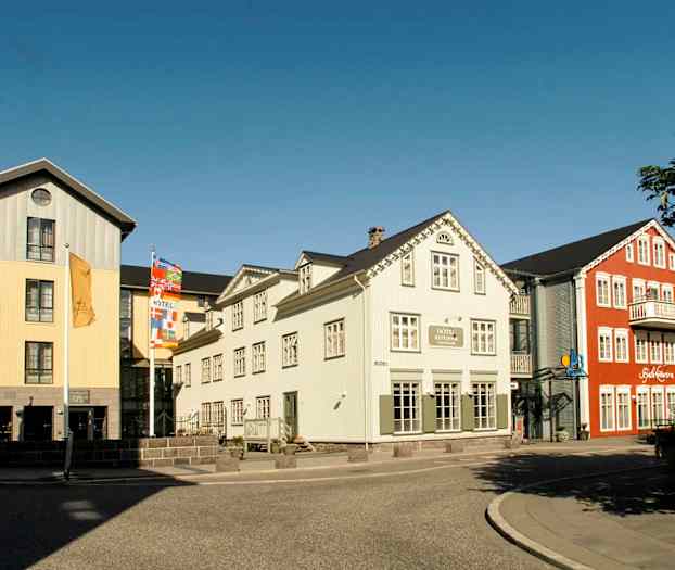 Bild av färgglada byggnader med hotell och restaurang nära en gata med trottoar. (AI-genererad text)