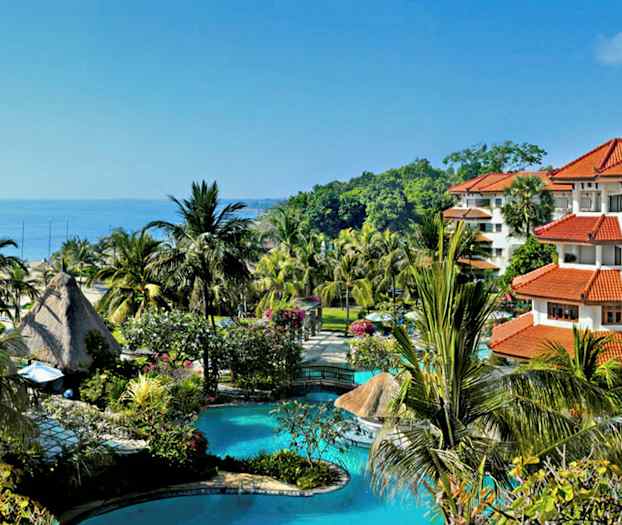 Bild av en tropisk semesterort med en pool, palmer och byggnader med röda tak, belägen nära havet. (AI-genererad text)