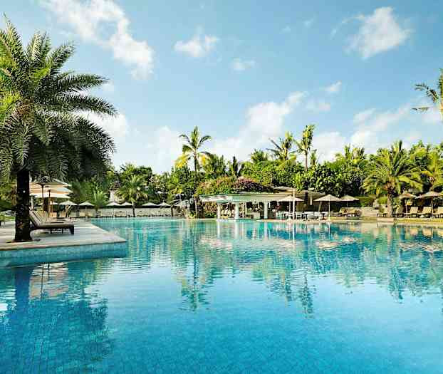 En stor pool omgiven av solstolar, parasoller och palmer, med en klarblå himmel i bakgrunden. (AI-genererad text)