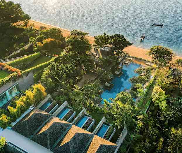 En fågelperspektivbild av ett strandnära lyxhotell med pooler, gröna trädgårdar och stranden som gränsar till havet. (AI-genererad text)