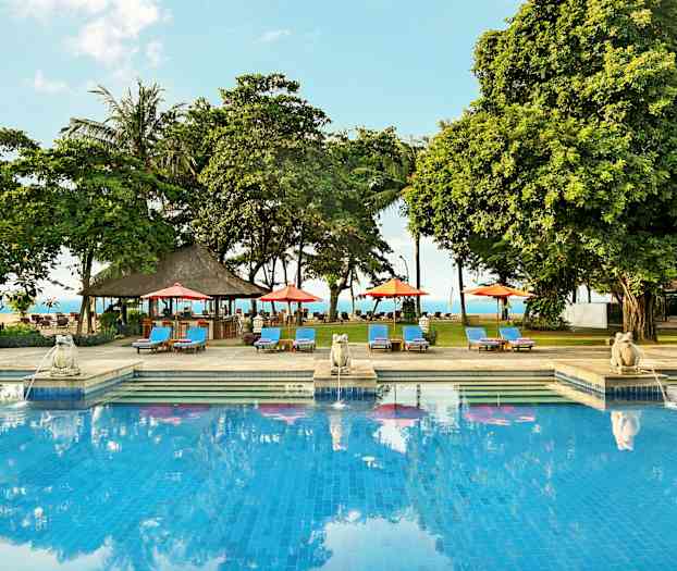 En utomhuspool omgiven av solstolar, parasoller och träd med havet i bakgrunden. (AI-genererad text)