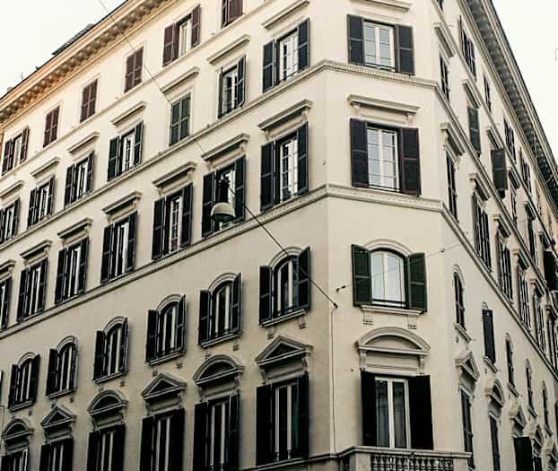 En hörnbyggnad med klassisk arkitektur och mörka fönsterluckor. (AI-genererad text)