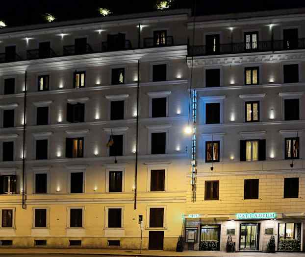 Ett kvällsbelyst flerbostadshus med en hotellskylt och upplysta fönster. (AI-genererad text)