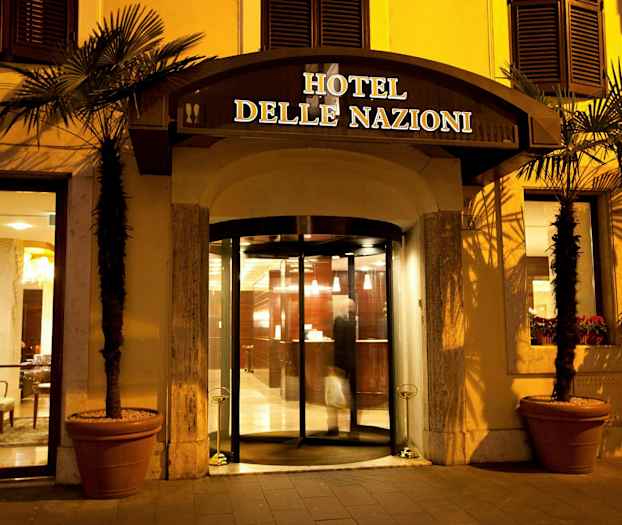 Entrén till Hotel delle Nazioni med glasdörrar och belysning på kvällen. (AI-genererad text)