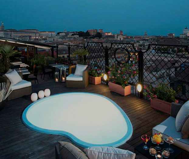 Bild på en takterrass med liten pool och sittmöbler, samt utsikt över en stad i skymning. (AI-genererad text)