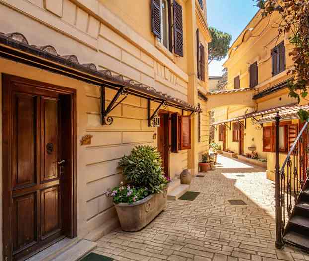 En solig innergård med jordsmutsgula byggnader, trappor och blomplanteringar. (AI-genererad text)