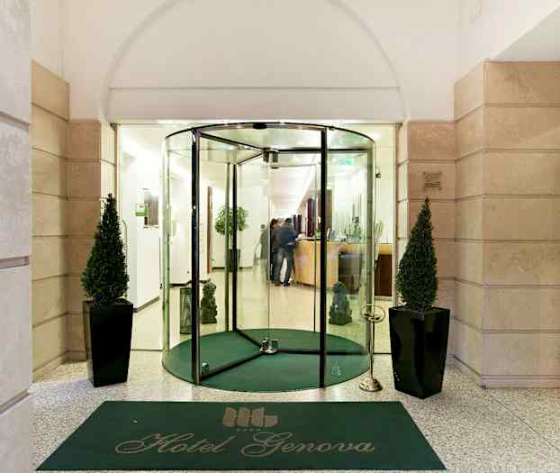 Entrén till Hotel Genova med glasdörrar, grön matta och två dekorerade växter. (AI-genererad text)