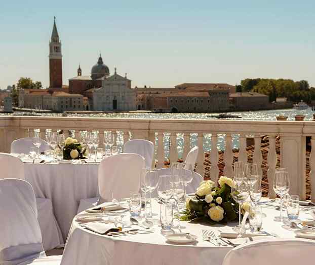 En utomhusmiddag på en terrass med utsikt över en historisk byggnad vid vattnet. (AI-genererad text)