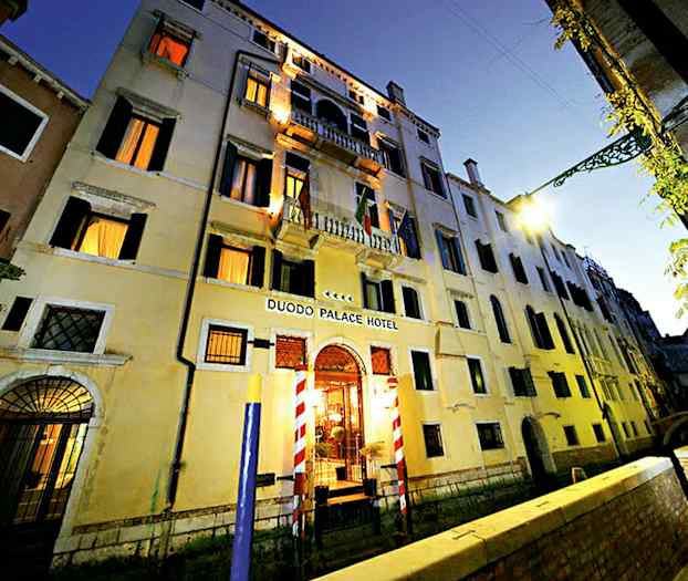 Flerbostadshus i tre våningar med skylt Duodo Palace Hotel, omgivna av en kanal och en gångväg. (AI-genererad text)