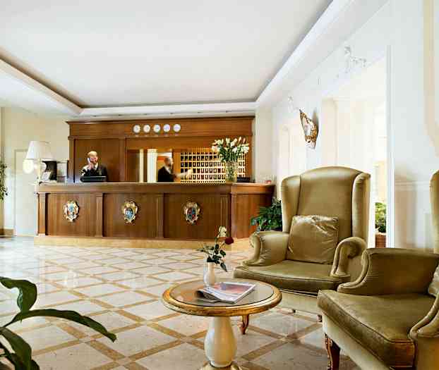 Ett hotellreceptionområde med en reception i trä och sittplatser med gröna fåtöljer. (AI-genererad text)