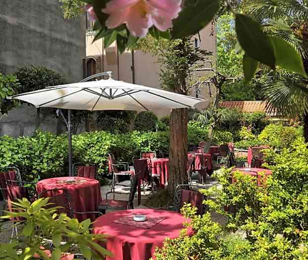 En grönskande innergård med röda bord och stolar samt ett stort vitt parasoll. (AI-genererad text)
