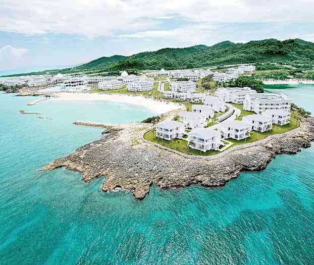 Flygvy över ett kustlandskap med vita byggnader omringade av grönska och turkost vatten. (AI-genererad text)