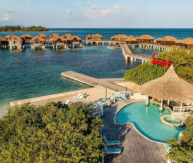 Flytande bungalows på stolpar i havet med en pool och solstolar i förgrunden. (AI-genererad text)