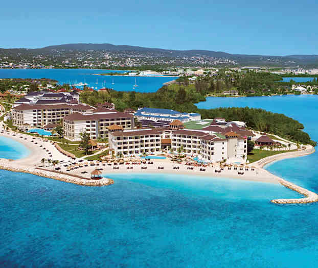 En resort belägen vid havet med stränder och pooler, omgiven av grönska och blått vatten. (AI-genererad text)