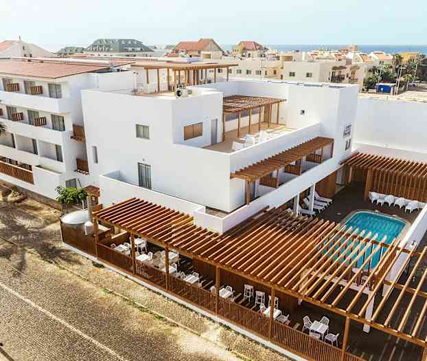 Flerbostadshus med vit fasad, trädetaljer och utomhuspool. (AI-genererad text)