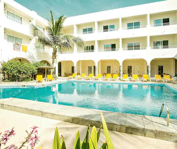 En utomhuspool med gula solstolar och en vit byggnad med balkonger. (AI-genererad text)