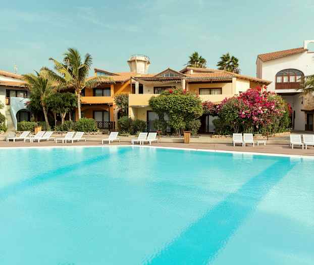 Utomhuspool vid semesteranläggning med omgivande byggnader och grönska. (AI-genererad text)