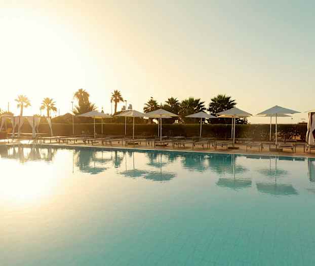 Poolområde med solsängar och parasoller vid solnedgång. (AI-genererad text)