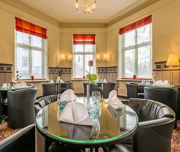 Interiör av en restaurang med dukade runda bord och stora fönster. (AI-genererad text)