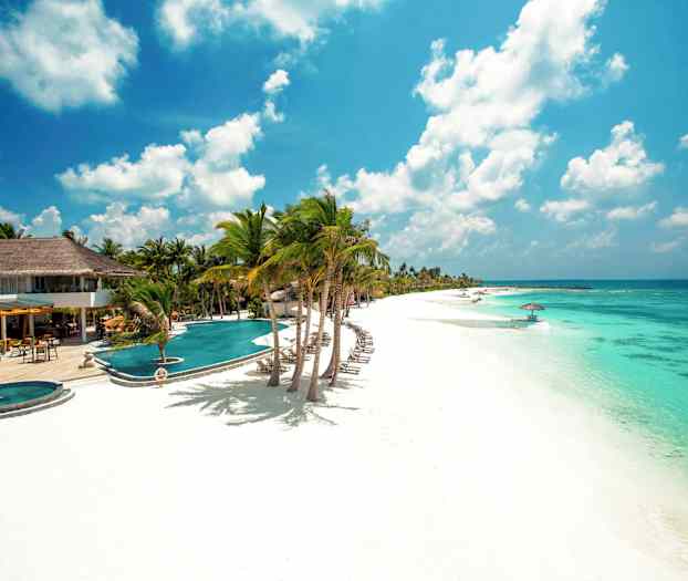 Bild av en vit sandstrand med turkost vatten, solstolar, parasoller och palmträd vid ett hotellområde. (AI-genererad text)