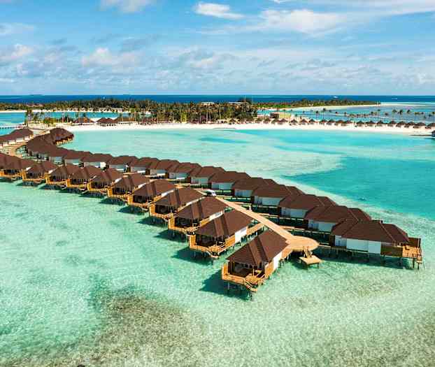 Bungalows över vatten med en tropisk strand i bakgrunden. (AI-genererad text)