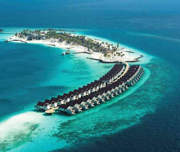 Flygfoto av en ö med strand, palmer och bostäder byggda över vatten. (AI-genererad text)