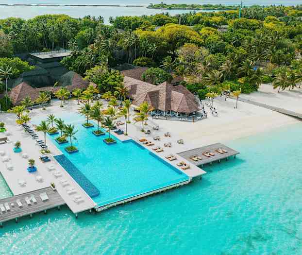 En resort med en pool som ligger precis vid turkosblått vatten, omgiven av palmer och grönska. (AI-genererad text)