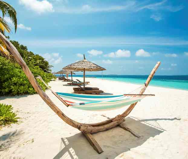 En strand med en hängmatta, parasoller och solstolar vid havet. (AI-genererad text)