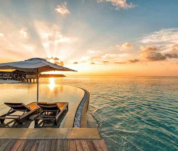 Två solstolar med parasoll vid en infinitypool och havet i solnedgången. (AI-genererad text)