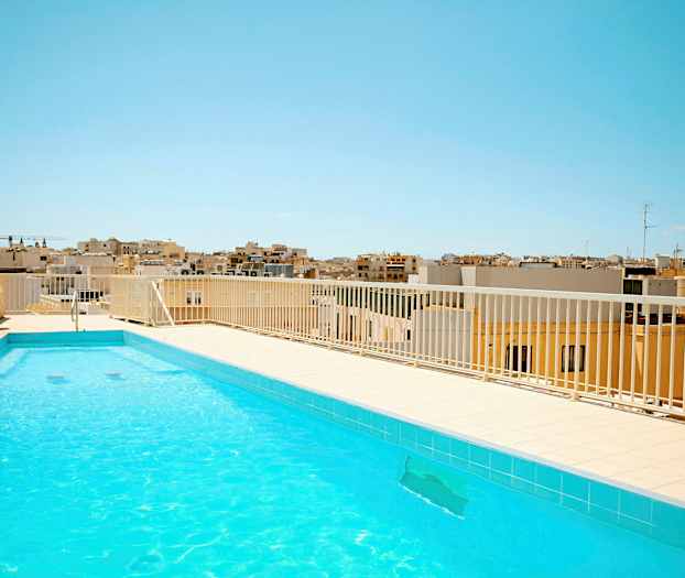 En utomhuspool med klart vatten på en takterrass. I bakgrunden syns stadsbebyggelse under en klar blå himmel. (AI-genererad text)