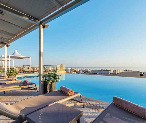 Solstolar vid en infinitypool med utsikt över en stad och havet. (AI-genererad text)