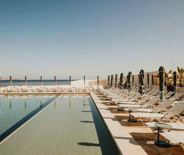 Bild av en pool med solstolar och parasoller i ett soligt utomhusområde. (AI-genererad text)