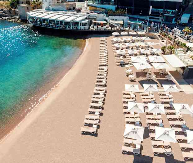 Strand med solstolar och parasoller samt en närliggande byggnad. (AI-genererad text)