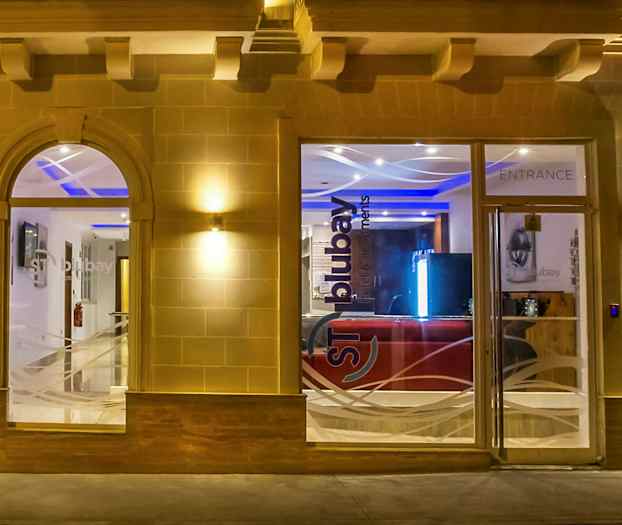 Entrén till en byggnad med glasfönster och dörrar, upplyst på kvällen. (AI-genererad text)