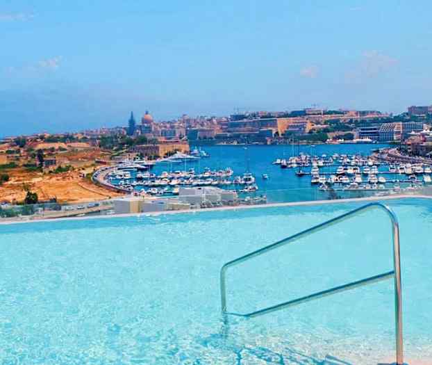 Utsikt över en pool med räcke, där en hamn med många båtar och stadsmiljö syns i bakgrunden. (AI-genererad text)