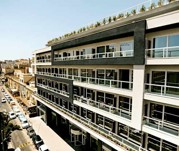 En flervåningsbyggnad med moderna balkonger längs fasaden, belägen vid en stadsgata. (AI-genererad text)