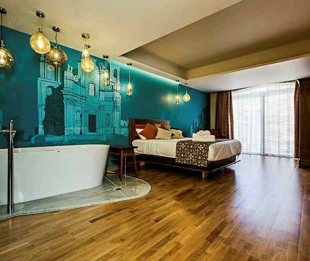 Ett hotellrum med en säng, ett fristående badkar, och blå väggmålningar. (AI-genererad text)